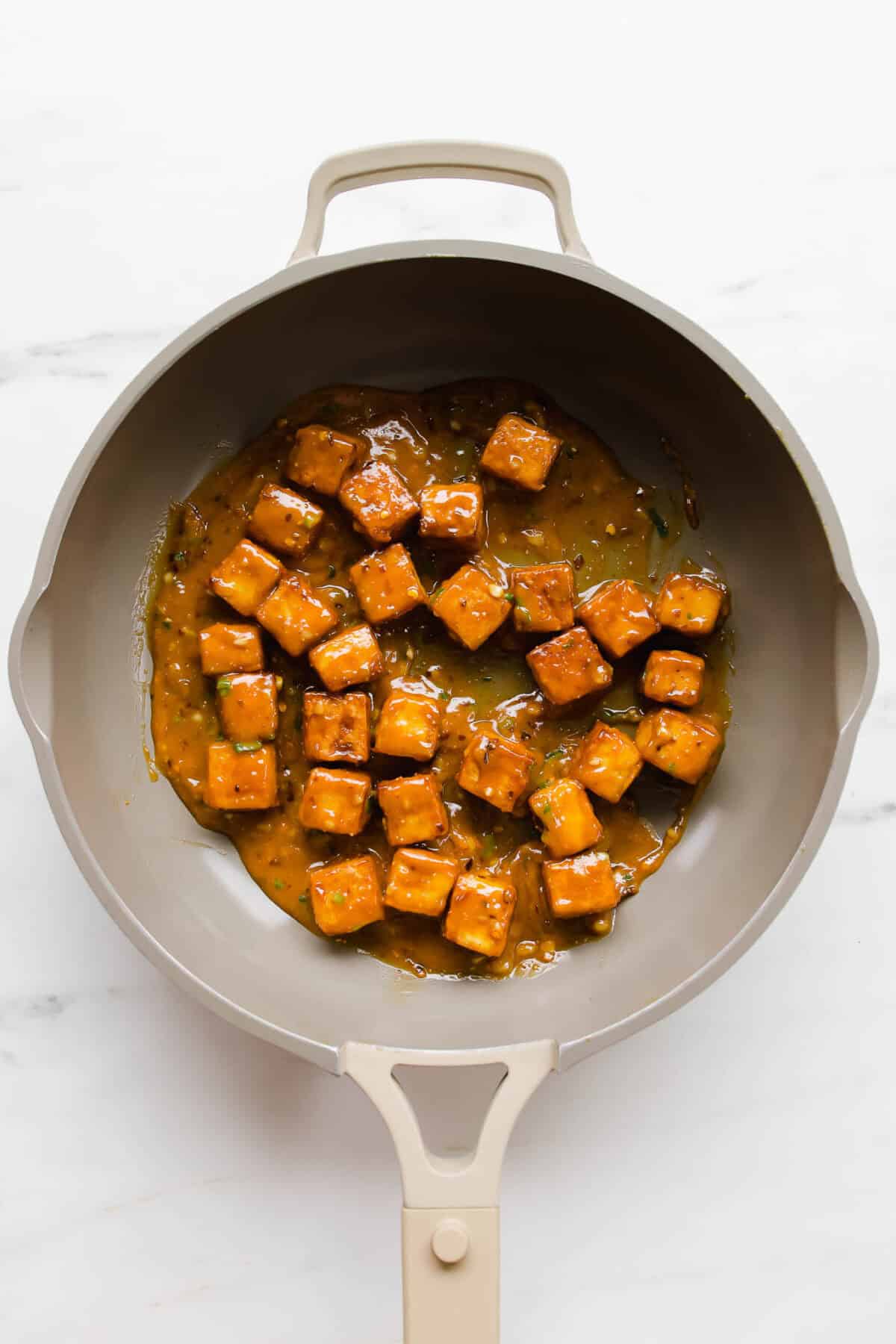 Cubes of tofu in peanut sauce in a taupe pan.