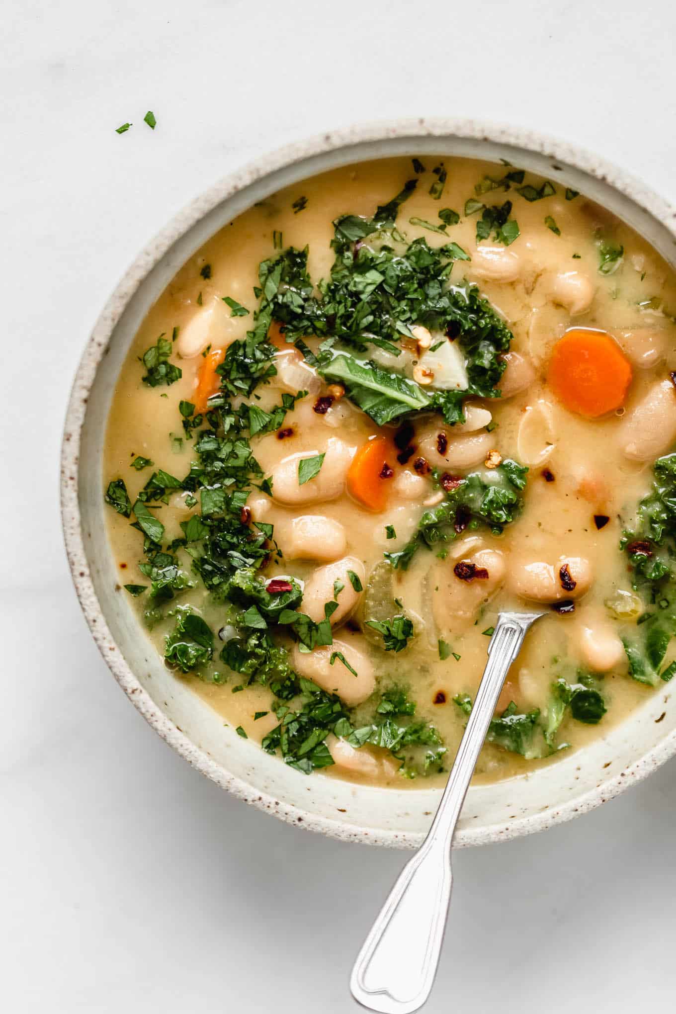 A bowl of tuscan white bean soup with a spoon in it.