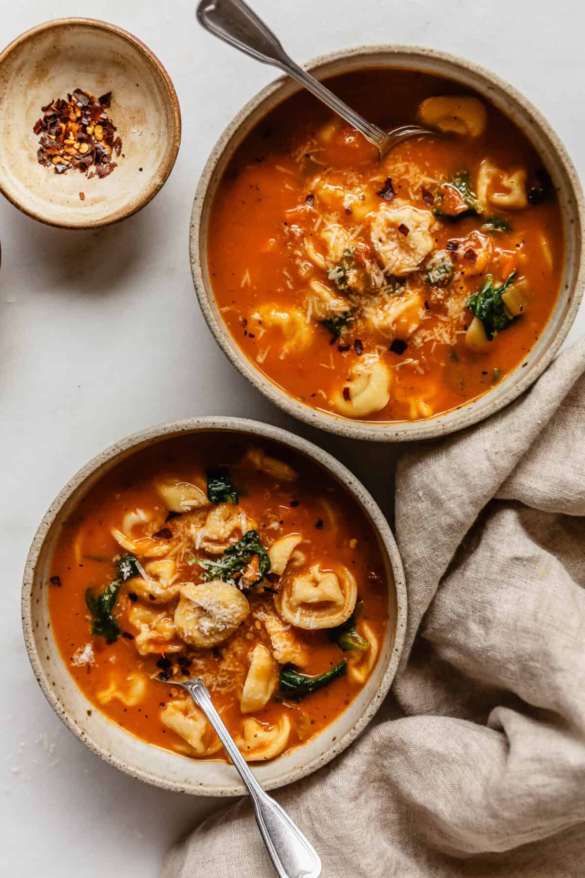 Two bowls of soup with tortellini and a beige napkin on the side.