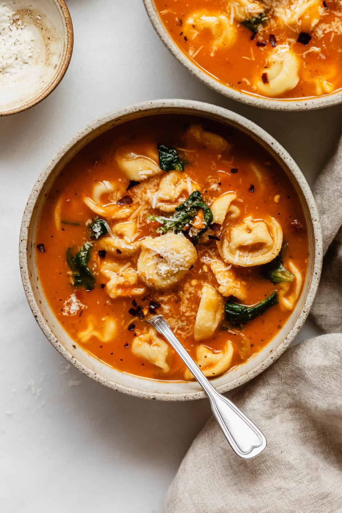 A bowl of tuscan tortellini soup with grated parmesan cheese on top.