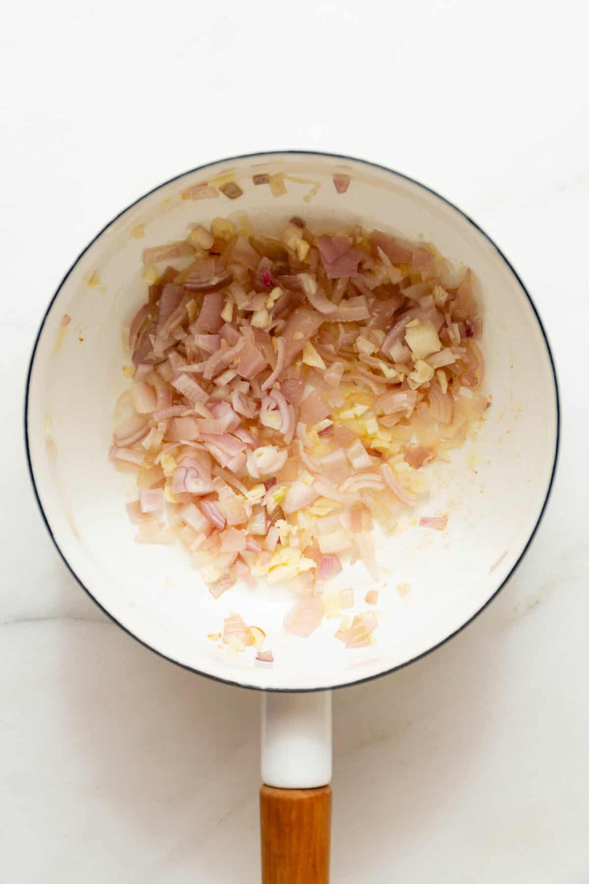 Sautéed shallots and garlic in a white pot.