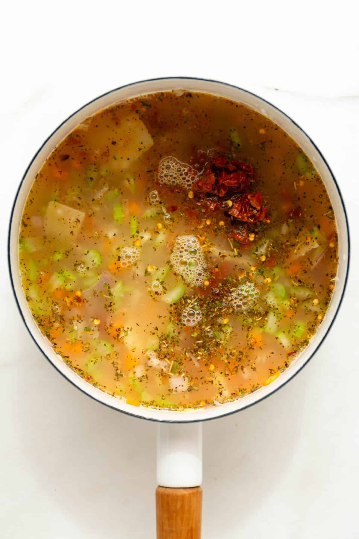 Tuscan soup broth in a white pot.