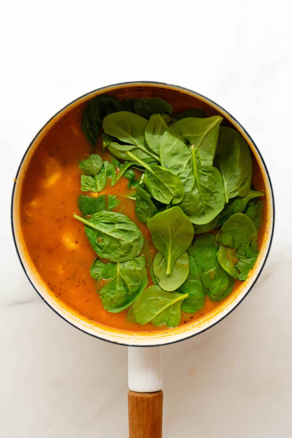 A pot of tortellini soup with fresh spinach in it.