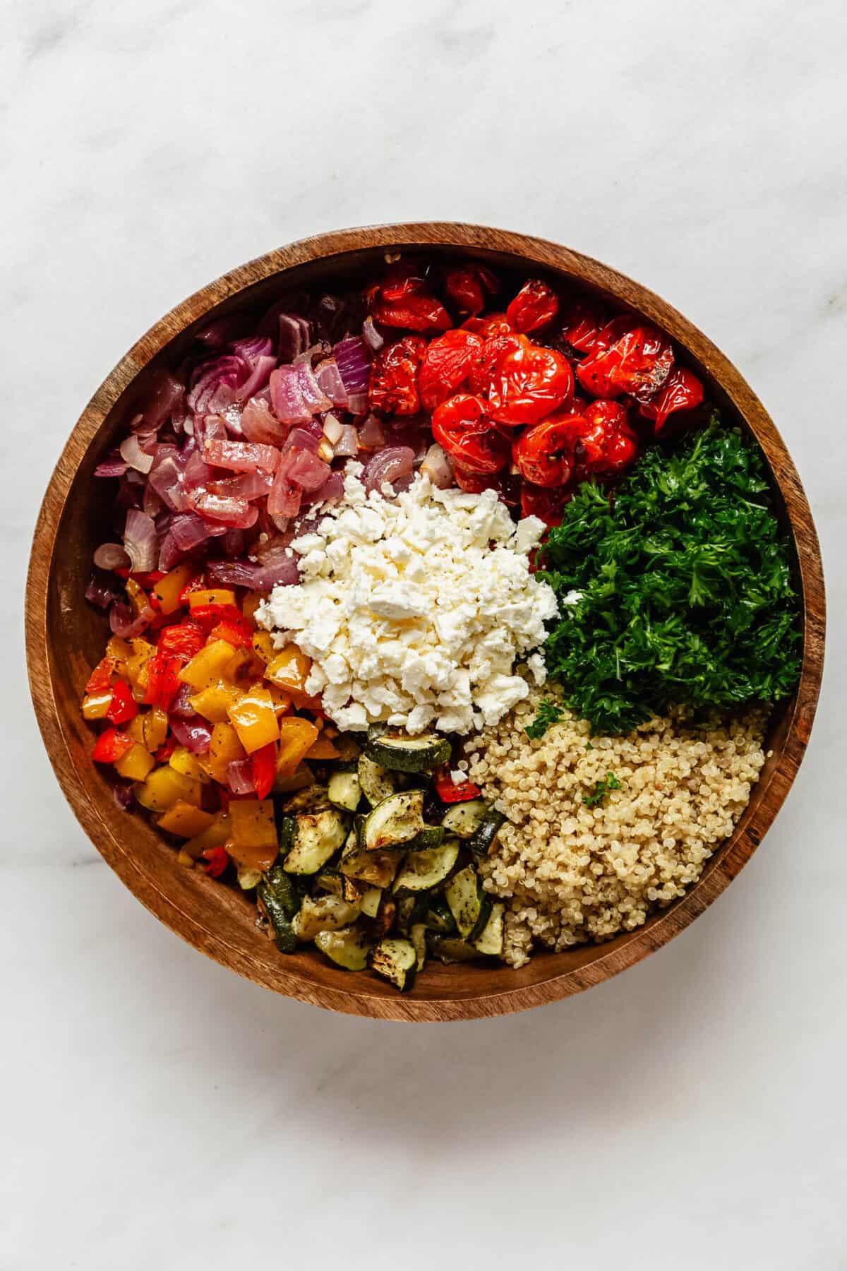 quinoa, roasted vegetables, feta, and parsley in a wood bowl.