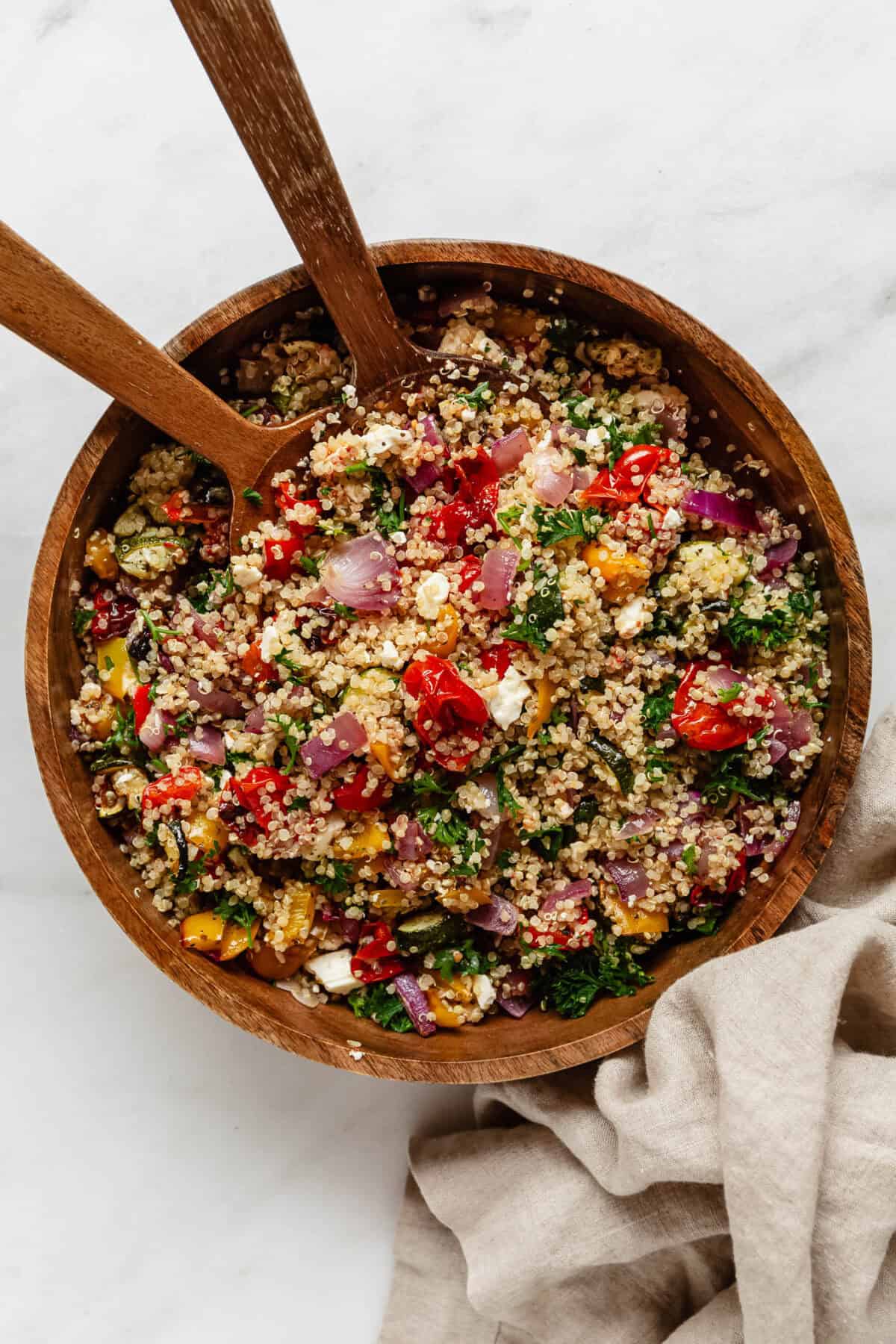 a wood bowl of roasted vegetable quinoa salad with wood serving spoons.